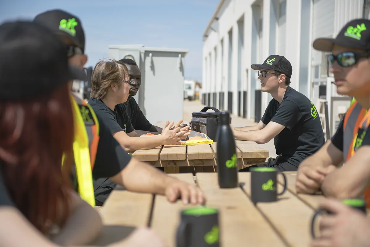 Des membres de l'équipe en uniforme sont assis à une table de pique-nique en plein air, engagés dans une conversation.