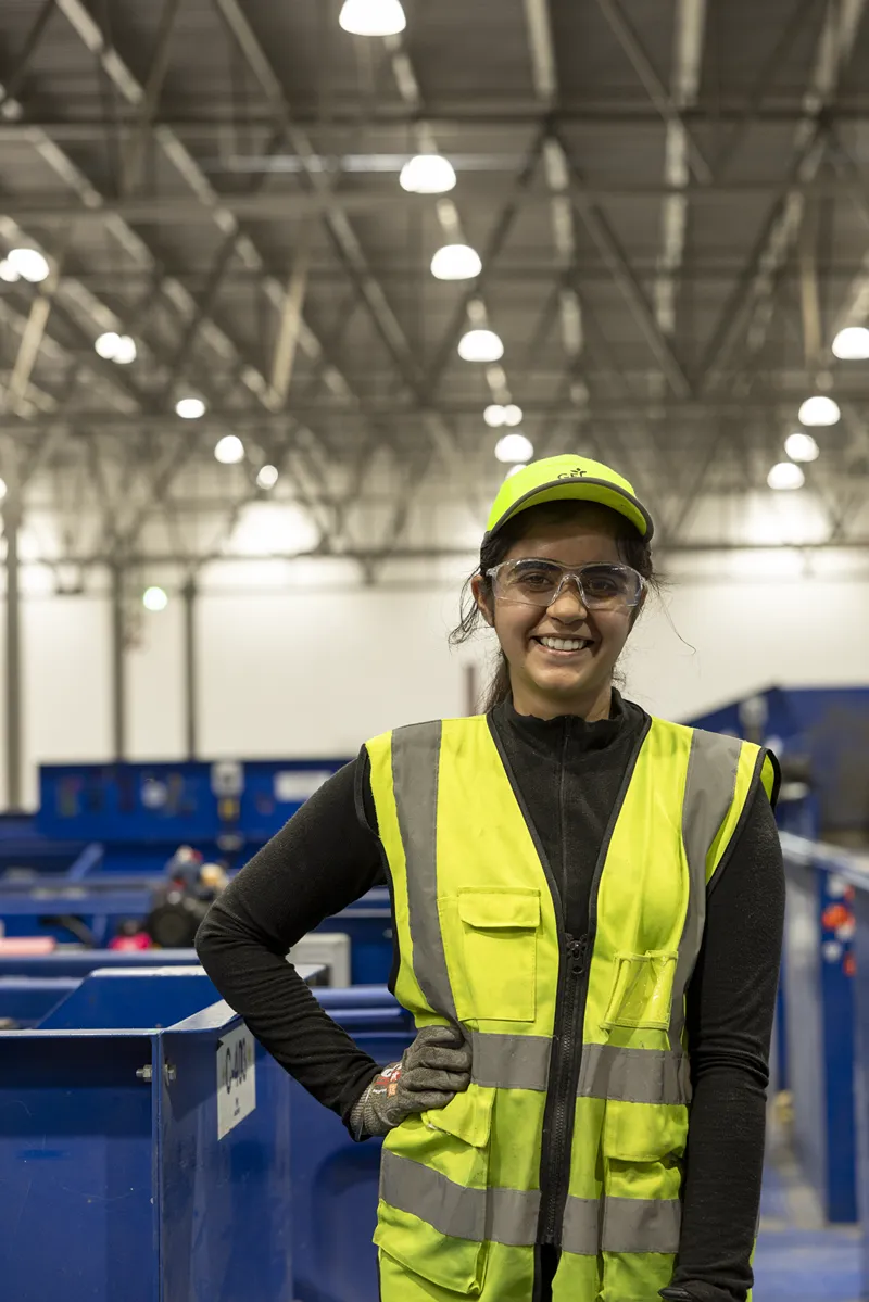 Femme souriante portant un gilet de sécurité et des lunettes dans un entrepôt Oppo.