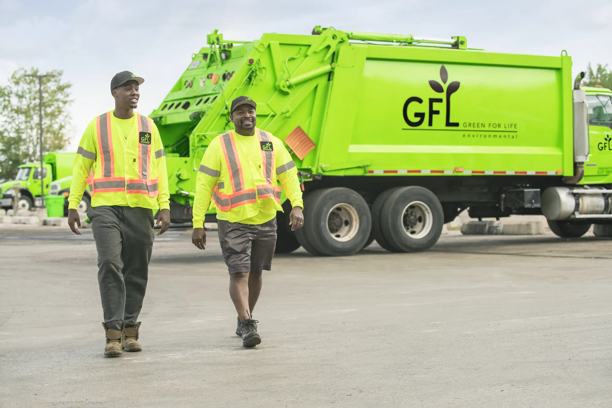 Three smiling workers in safety gear converse in a recycling plant