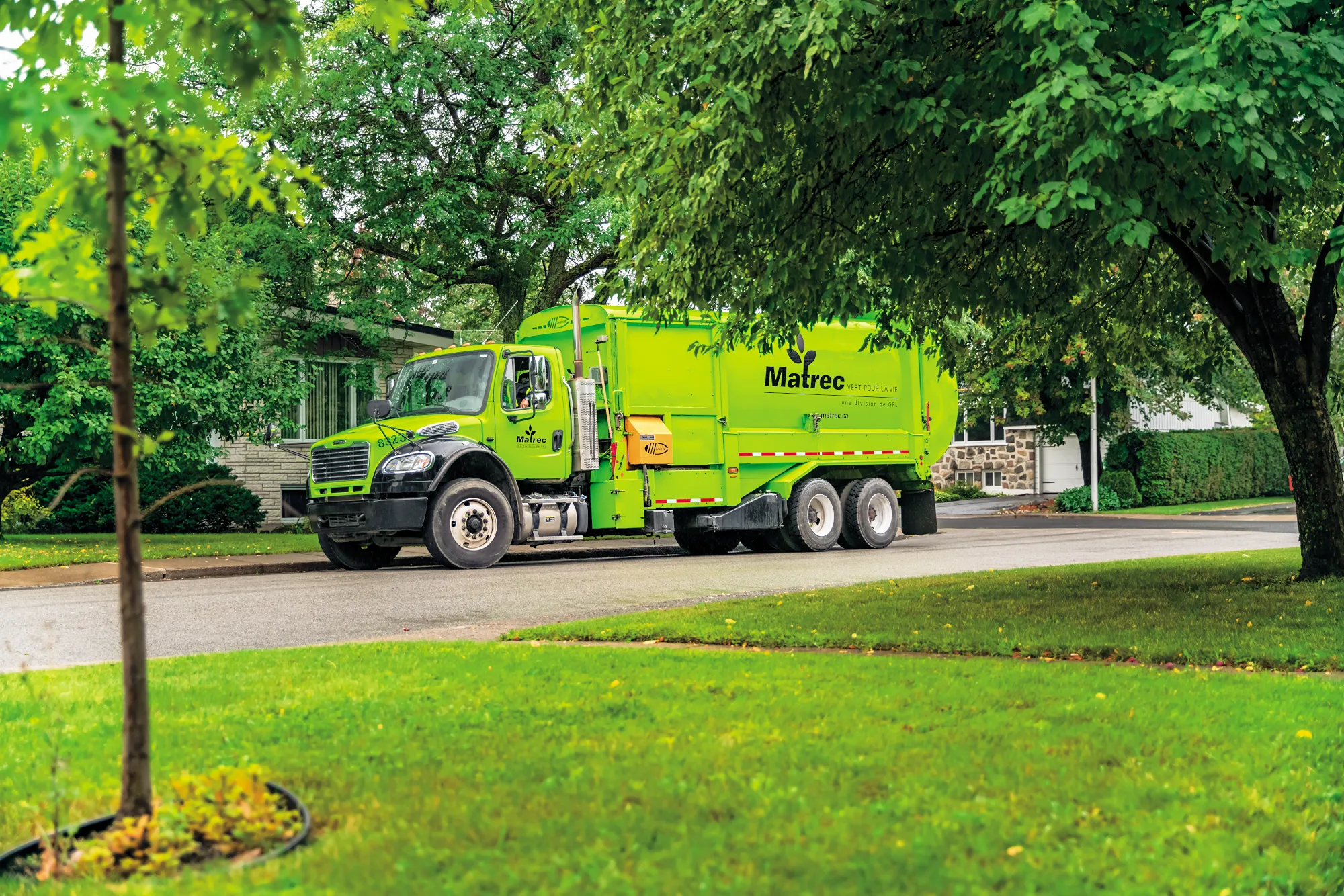 Camion poubelle vert vif roulant dans une rue de ville