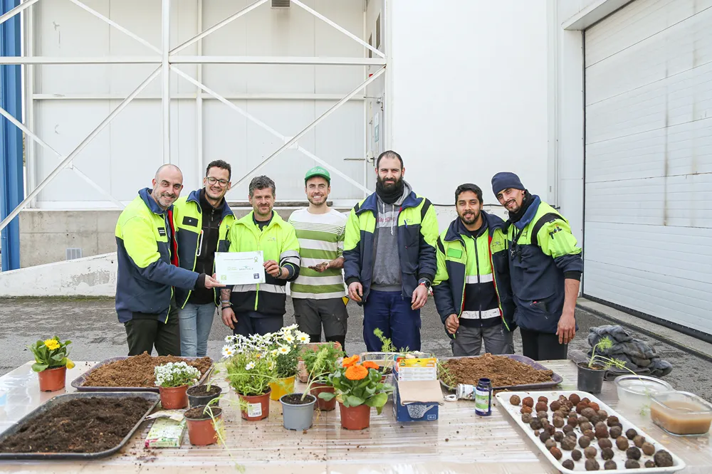 Group of people celebrating with plants and certificates outside building