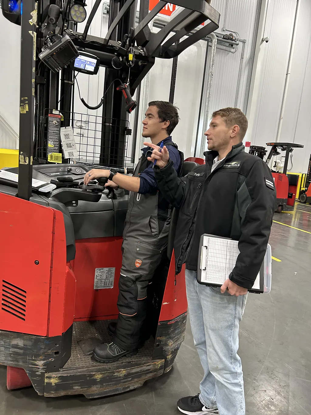 A female manager in a hard hat and safety vest uses a tablet to conduct a facility assessment in the warehouse.