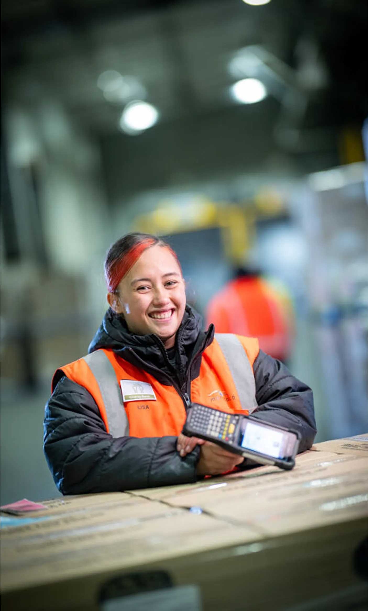Woman in safety vest smiling at camera holding scanner in warehouse setting