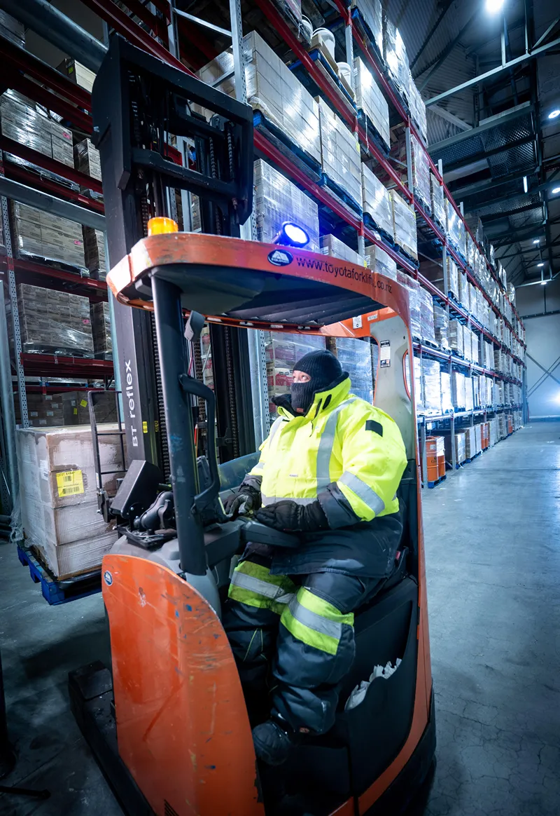 Warehouse worker operating a forklift in a cold storage facility, wearing high-visibility insulated gear for safety and warmth.