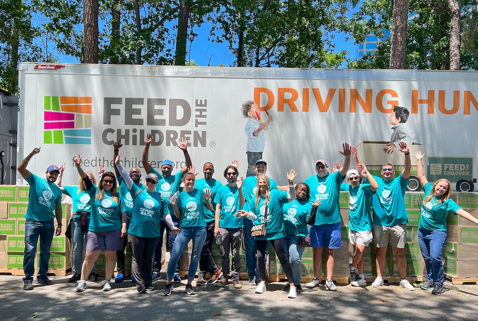 A group of people in teal shirts stands in front of a Feed the Children truck