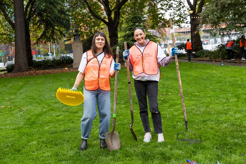 two volunteers in orange vests with a shovel and rake, participating in an environmental cleanup