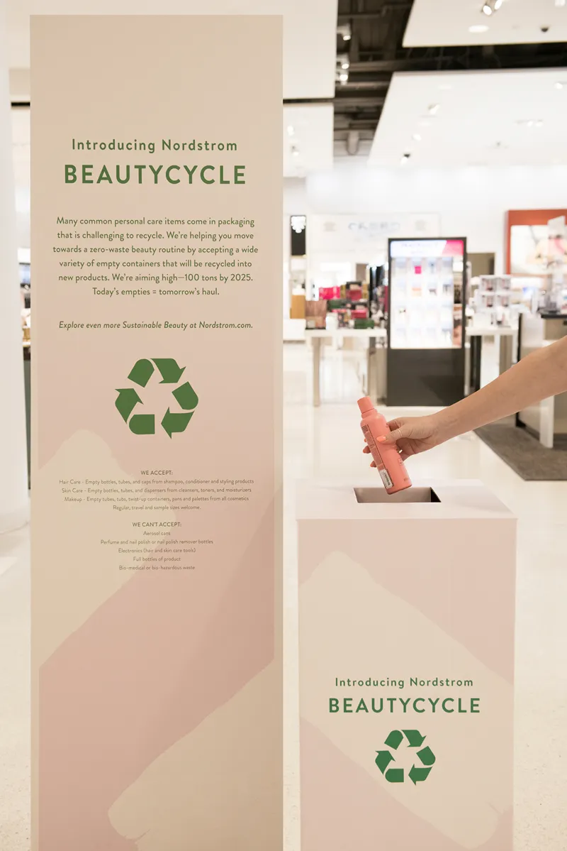 A person depositing a pink bottle into a Nordstrom BEAUTYCYCLE recycling bin