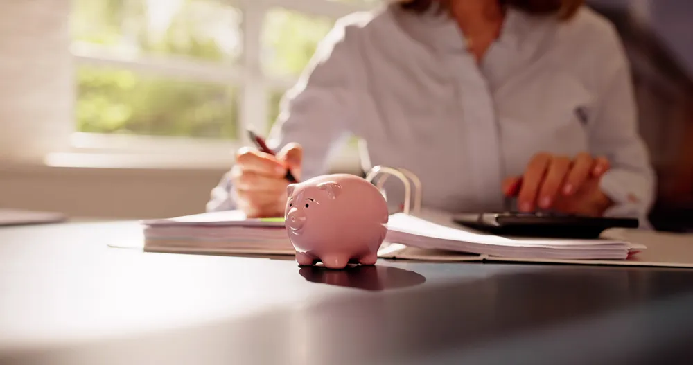 a woman is writing on a notebook and a piggy bank sits on the table