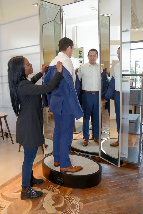 Sales associate helping a man try on a suit in a fitting room