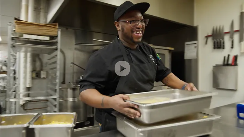 a man in a black shirt is smiling while holding a tray of food