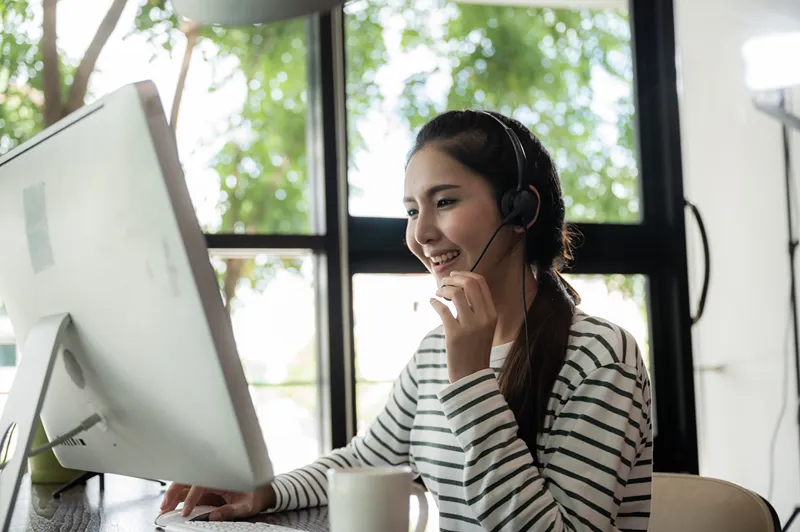 A friendly contact center representative is smiling while assisting a customer on a computer.