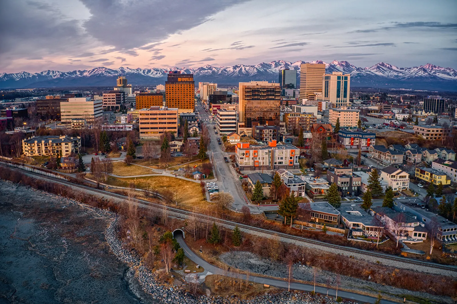 Aerial view of cityscape with snow-capped mountains in the background at dusk