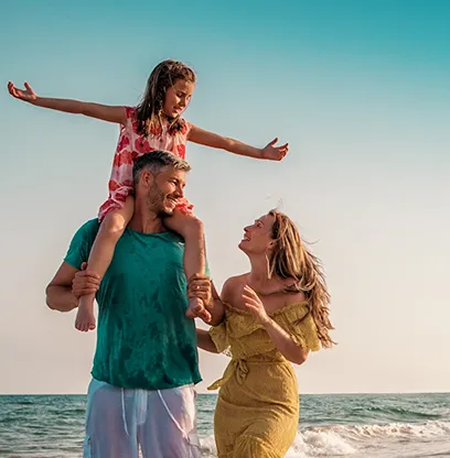 A family enjoys beach time with child on father's shoulders