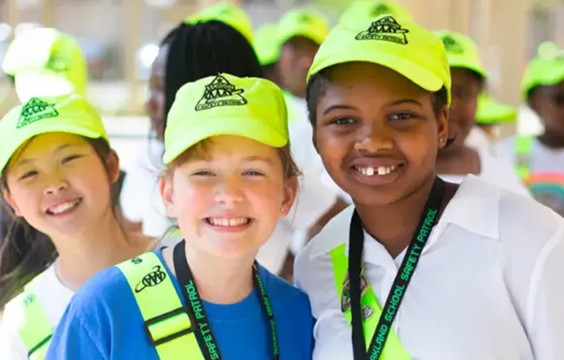 Children wearing bright green hats and safety vests smile together.