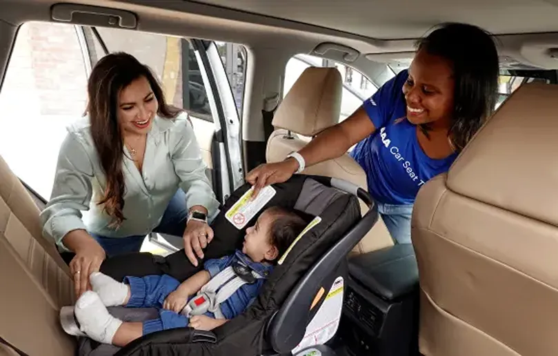 Two women secure baby in car seat inside vehicle