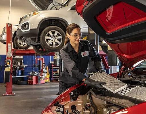 Woman in garage fixing car air filter with lifted vehicle above