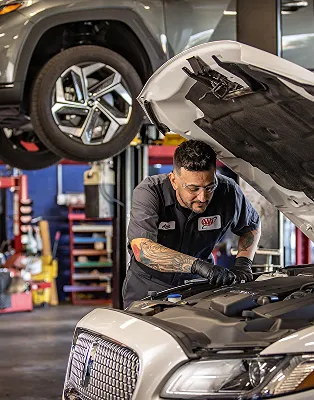 Mechanic working on car engine in garage with lifted vehicle above