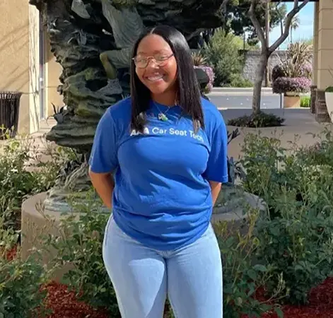 Woman in blue shirt smiling outdoors near fountain and plants