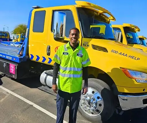 Man in safety vest stands next to yellow tow truck with "800-AAA-HELP" on side.