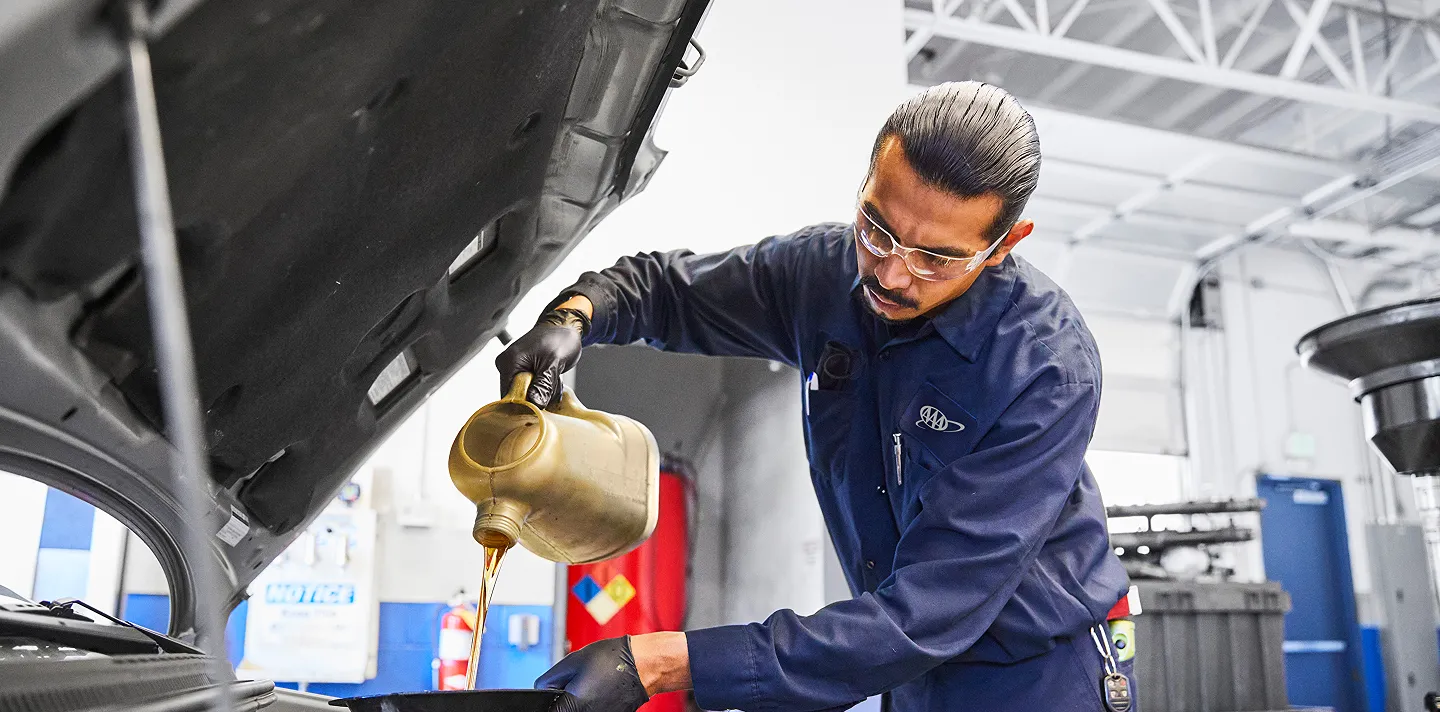 Mechanic pouring oil into car engine in garage
