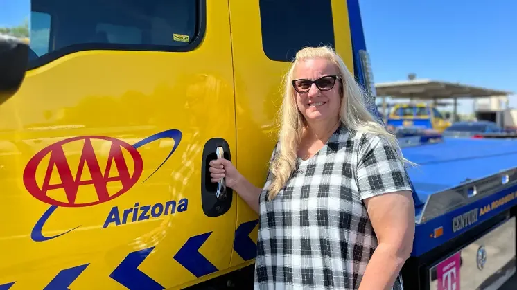Woman in plaid shirt stands next to AAA Arizona tow truck holding key