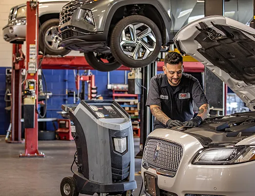 Mechanic working on car under lift in garage with diagnostic equipment nearby