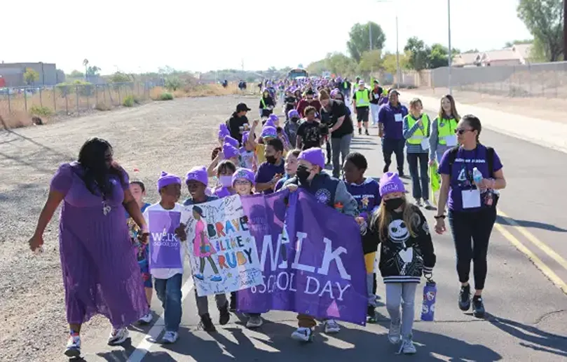 Children in purple walk with signs celebrating Walk to School Day