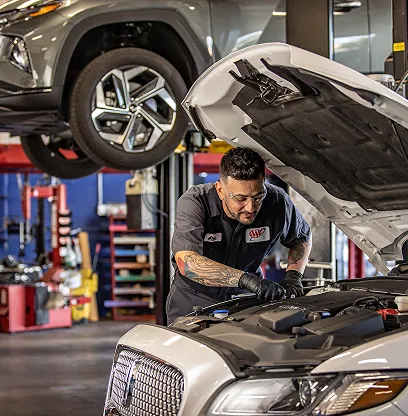 Mechanic working under car hood in garage with lifted vehicle above