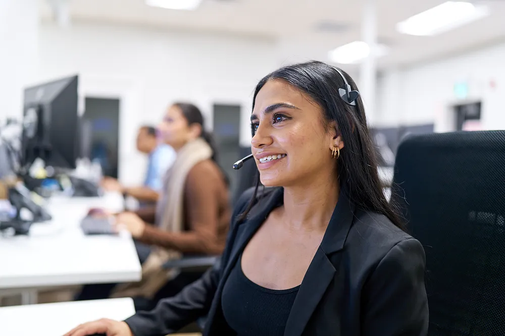 A smiling customer service representative is assisting a customer in a call center.