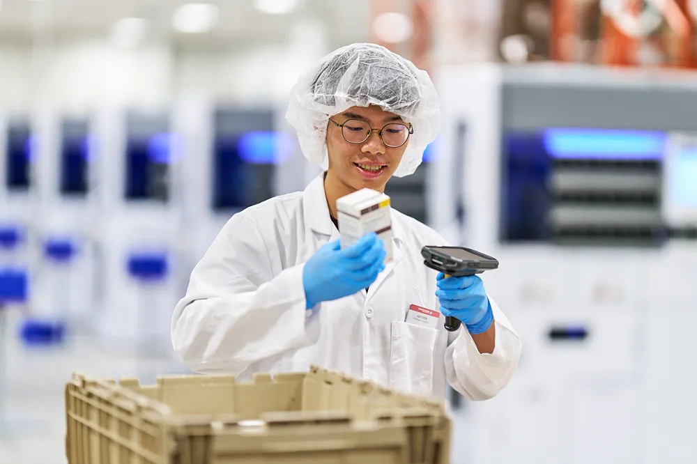 A young pharmacy technician is scanning a box of medication in a lab or distribution center.