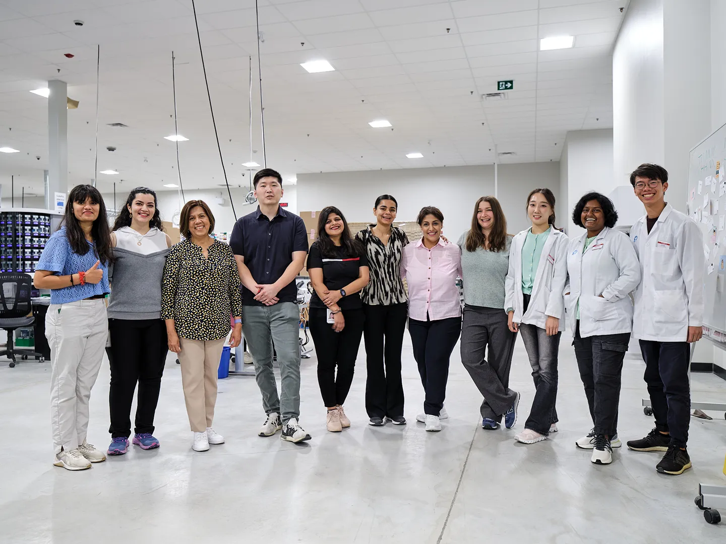A diverse group of cheerful central pharmacy employees is standing together in a brightly lit lab.