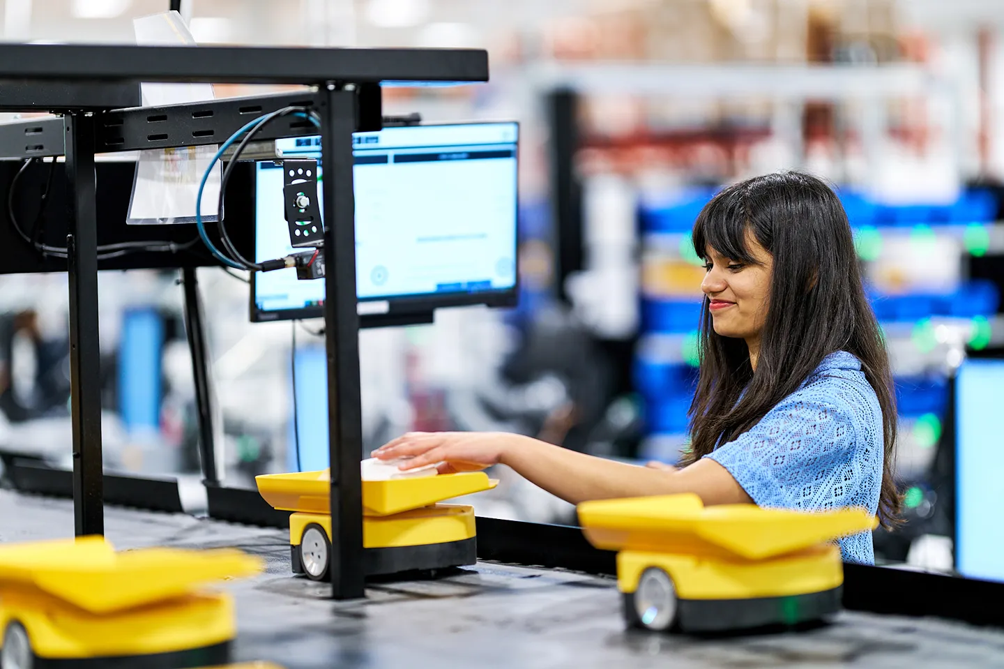 A female pharmacy technician is working with a conveyor system and small robots in a central fill pharmacy.