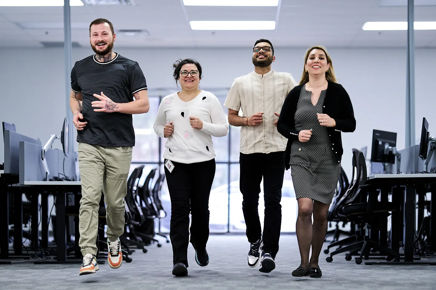 Four happy colleagues are smiling while walking together down an office aisle.