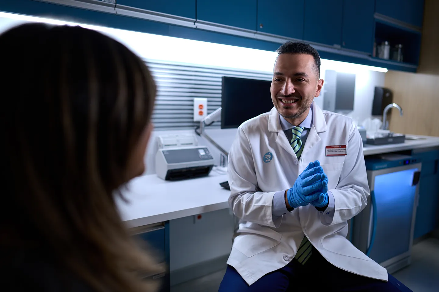 A professional in a lab coat is smiling while talking to a patient in a medical office.