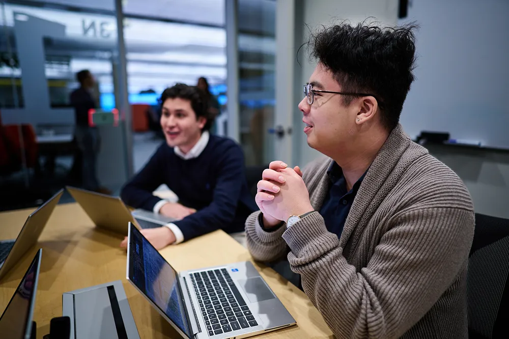 Two young professionals are working on their laptops while having a lively discussion