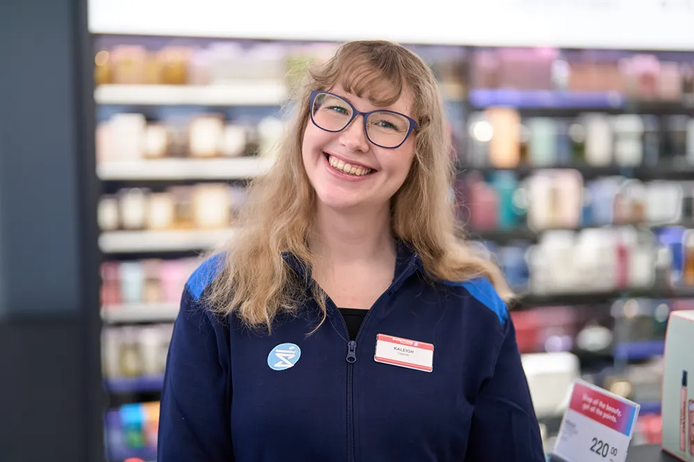 A happy retail associate wearing glasses is smiling at the camera in a store