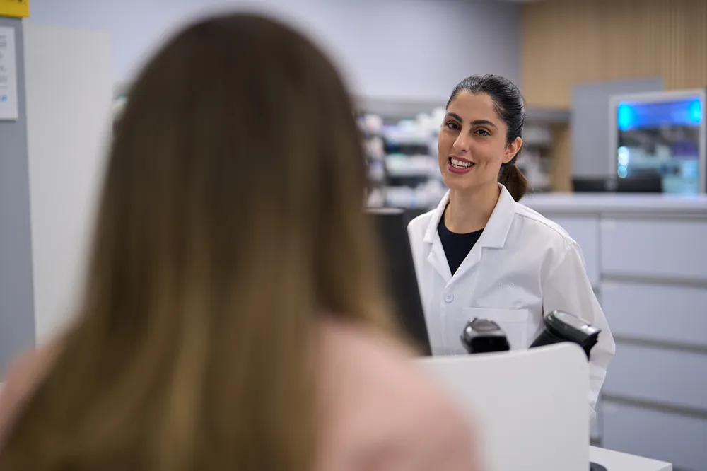 A smiling pharmacist is talking with a customer at a pharmacy counter