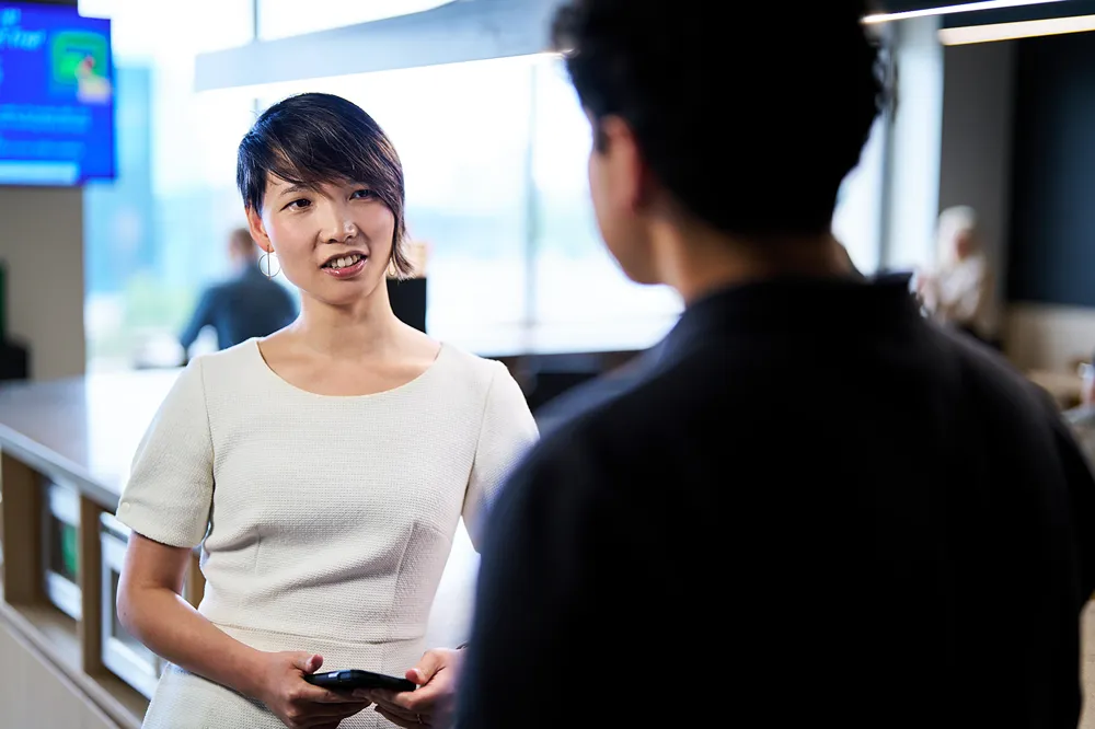 A professional is smiling while talking to a colleague during a meeting in an office