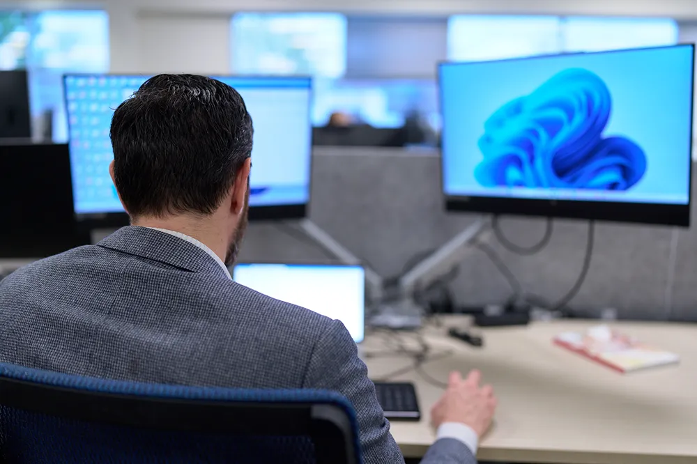A professional is focused while working on two computer monitors in a modern office