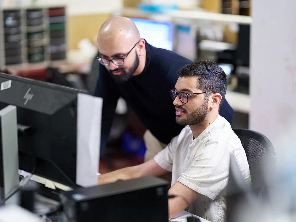 Two friendly IT professionals are collaborating on a computer in a corporate office.