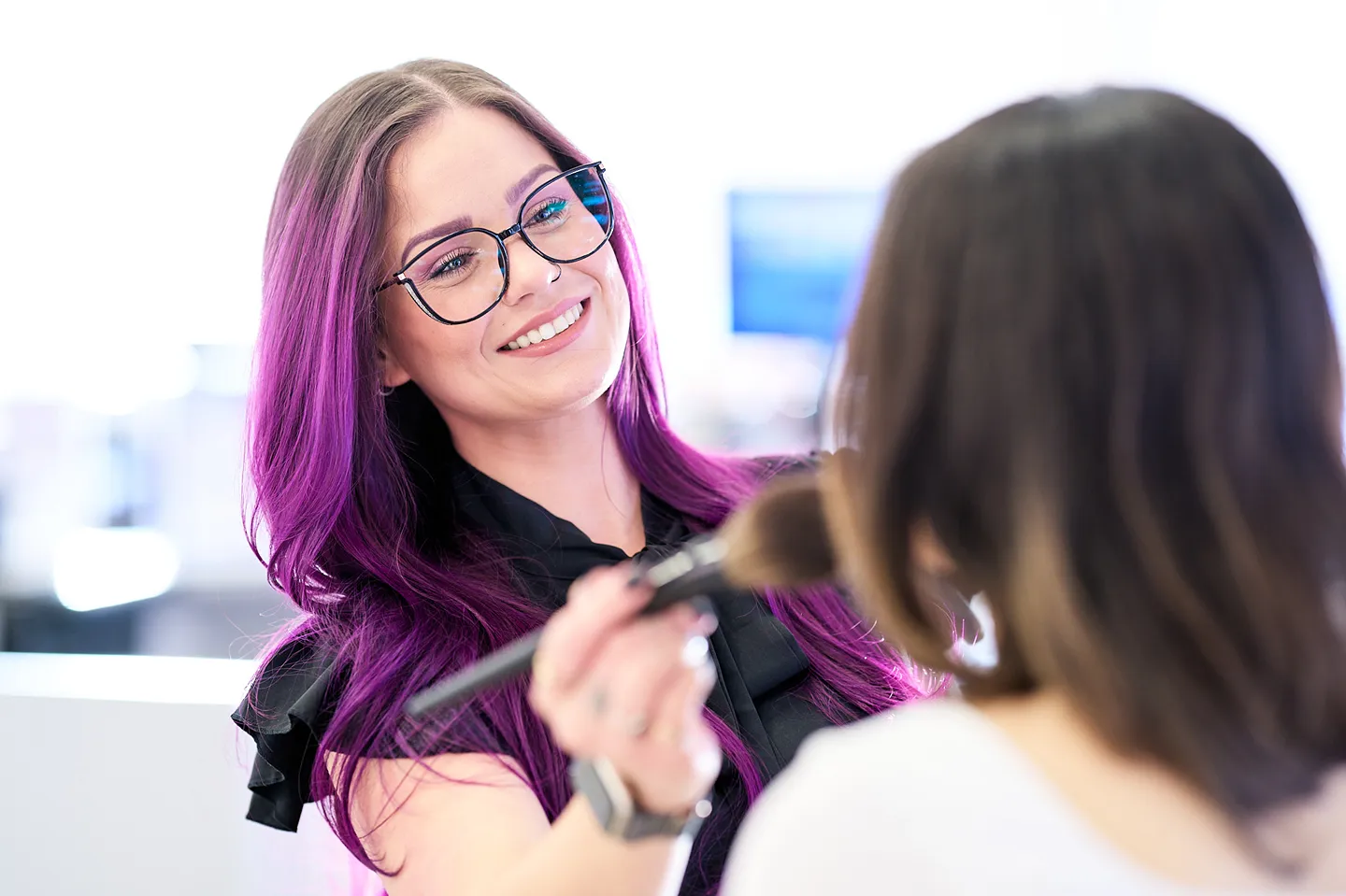 A smiling cosmetic sales associate is applying powder to a customer's face with a makeup brush