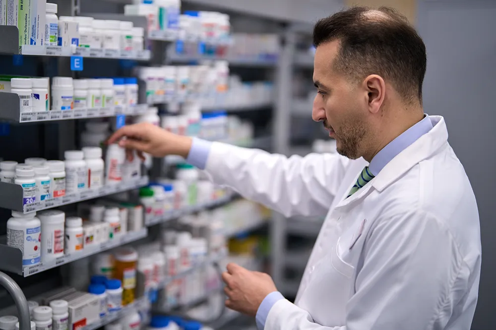 A professional pharmacist is stocking or retrieving medication from a shelf in a pharmacy.