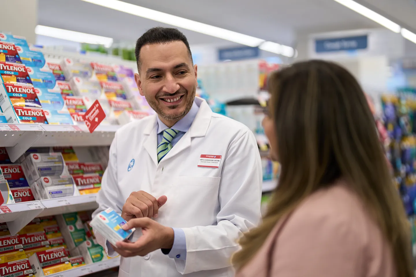 A smiling pharmacist is helping a customer with an over-the-counter medicine selection.