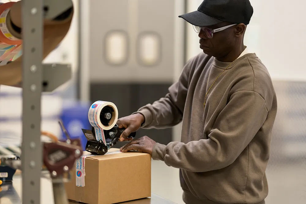A warehouse employee is carefully sealing a shipping box with packing tape