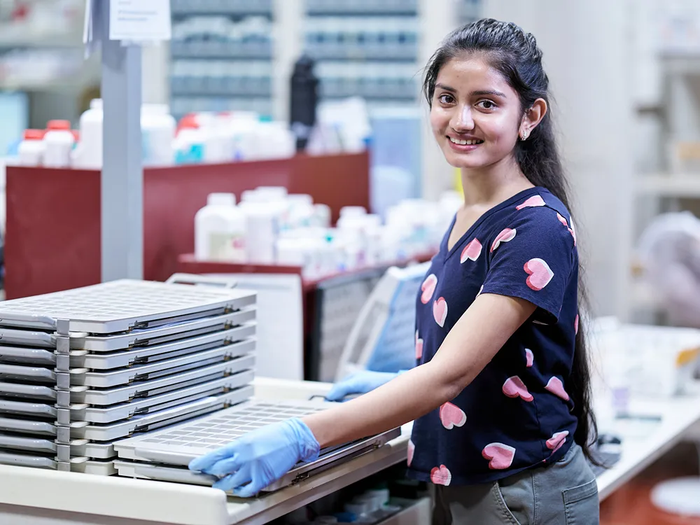 A smiling young professional is working with a pill packaging machine in a pharmacy.
