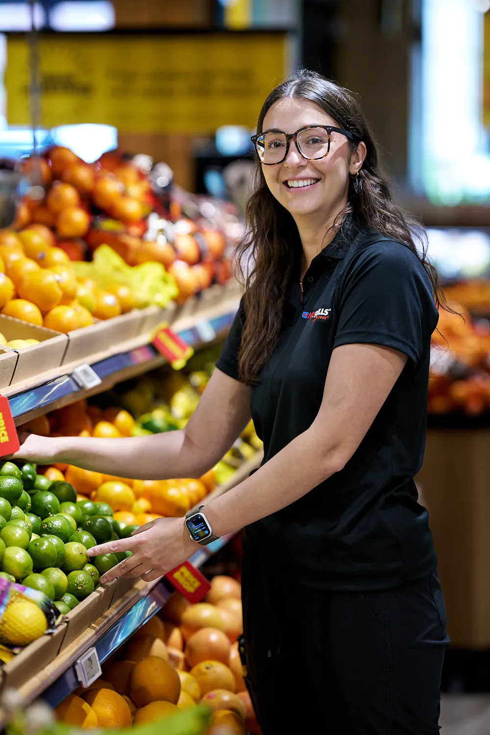 A friendly No Frills employee is smiling while stocking produce in a grocery store.