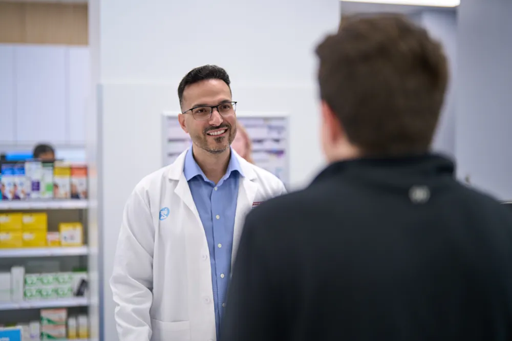 A friendly male pharmacist is smiling while assisting a customer at a pharmacy counter