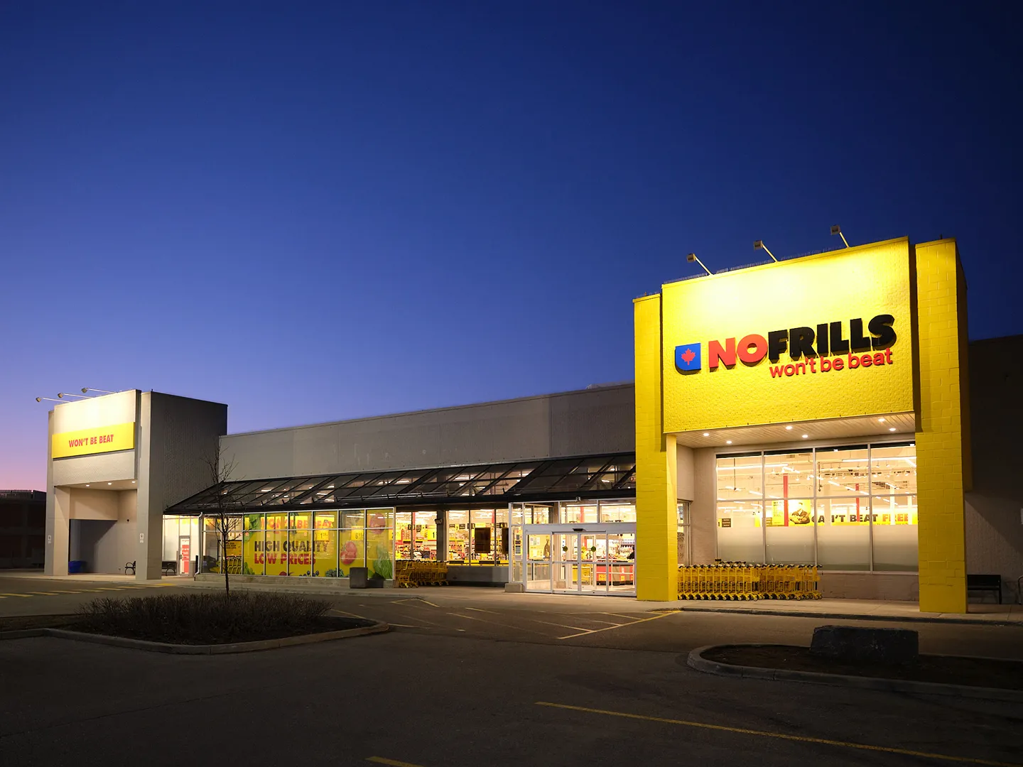 The exterior of a No Frills grocery store is illuminated at dusk.