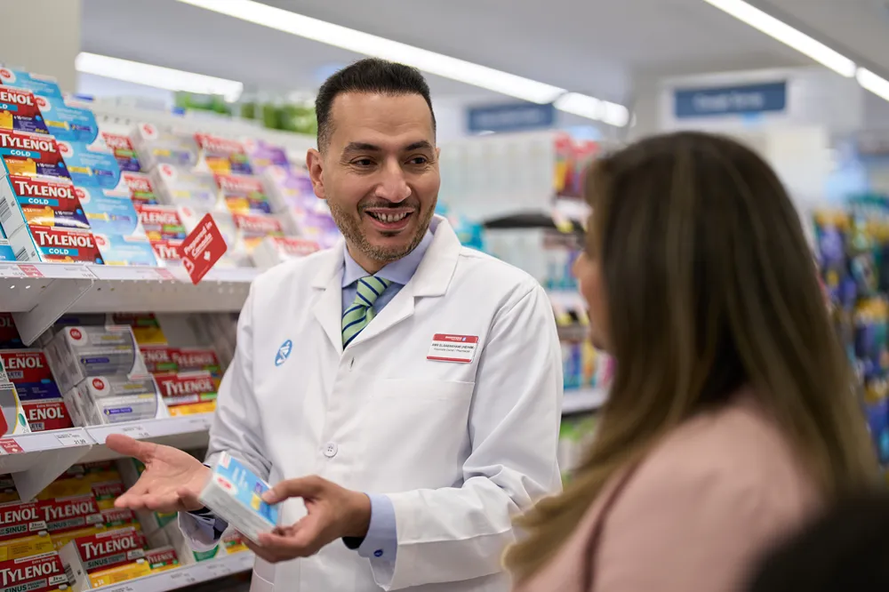 A friendly pharmacist is smiling while helping a customer find over-the-counter medicine