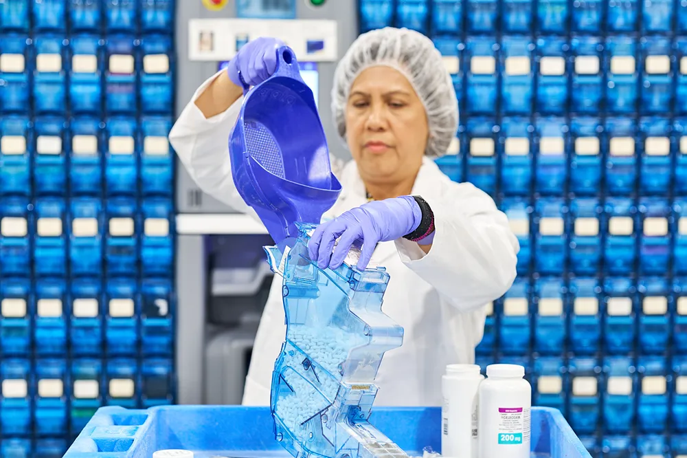 A pharmacy technician is carefully pouring pills into a counting machine in a centralized pharmacy